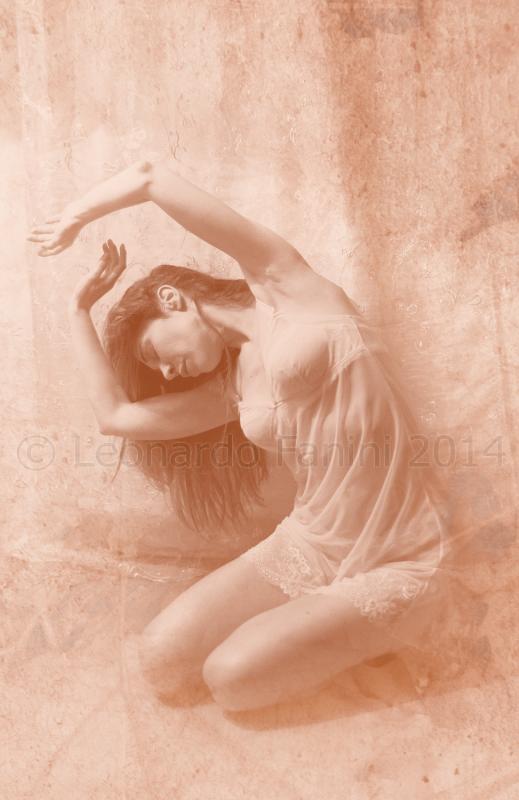 Sepia-toned artistic photograph of a woman in a flowing pose with her arms raised gracefully, evoking a sense of delicate movement.