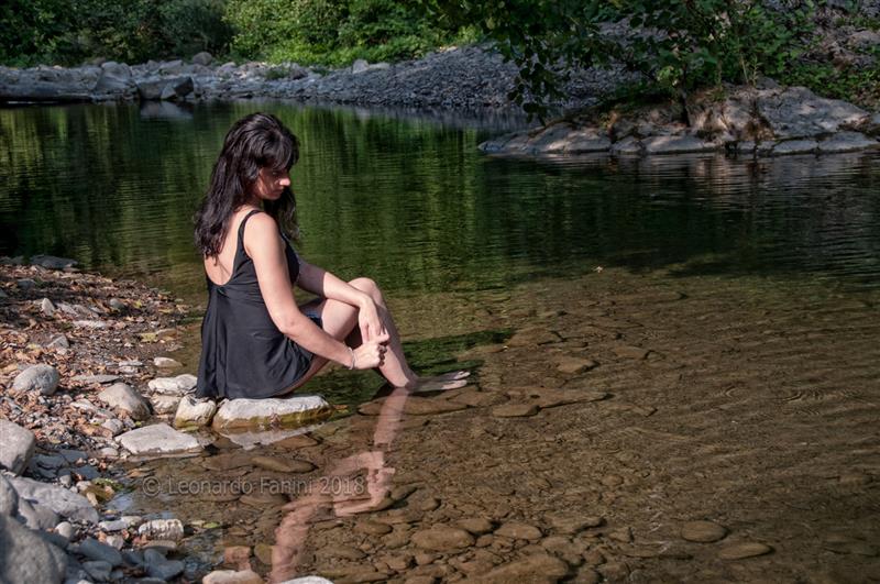 Ragazza seduta su una roccia lungo il Bisenzio, con i piedi nell
