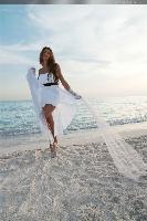 Woman in white flowing dress walking along the beach, with the ocean in the background, capturing a sense of elegance and freedom.